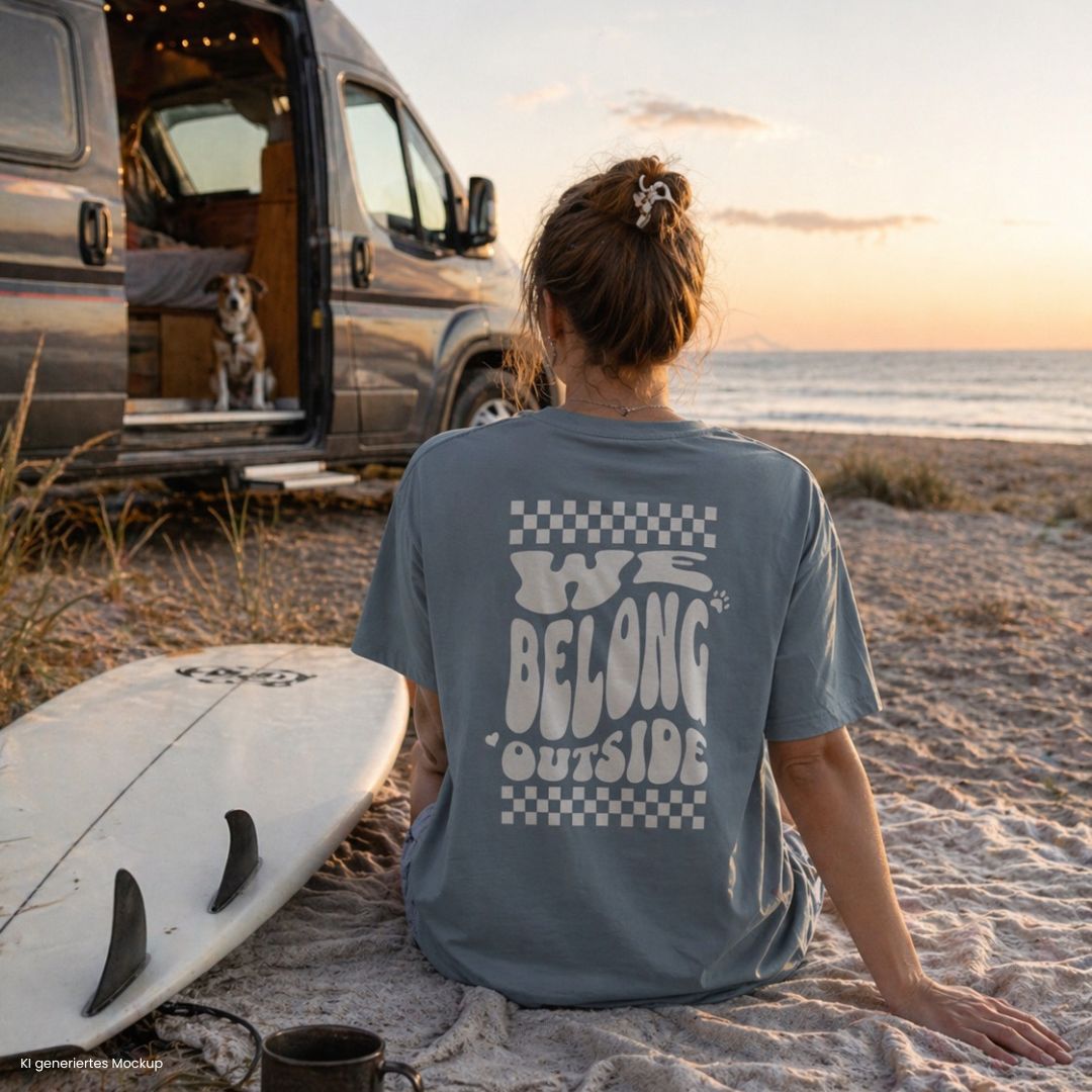 Person sitzt am Strand neben Camper und Hund und trägt ice blue „we belong outside“ T Shirt, ideal für Vanlife, Camping und Outdoor mit Hund