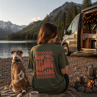 Person sitzt am See neben Camper mit Hund und trägt grünes „we belong outside“ T Shirt, perfekt für Camping, Vanlife und Outdoor mit Hund