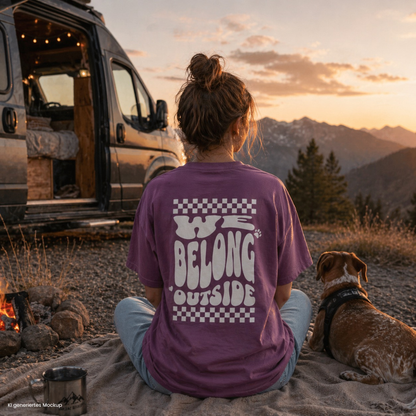 Person sitzt vor Camper mit Hund am Lagerfeuer in den Bergen und trägt lilafarbenes „we belong outside“ T Shirt, ideal für Camping und Vanlife