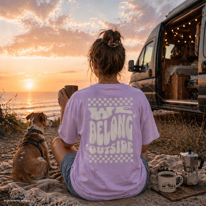 Person sitzt am Strand beim Sonnenuntergang neben Camper und Hund und trägt orchidfarbenes „we belong outside“ T Shirt, ideal für Vanlife und Camping